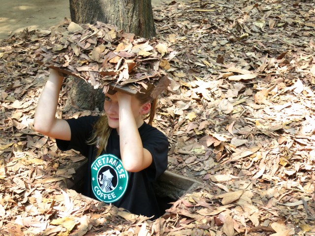 This is a picture of Ally standing in a camouflaged  trap door at the Cu Chi Tunnels.