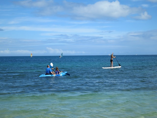 Chris and Kylee riding in a sea kayak, and Ally paddling on a paddle board, in Noumea